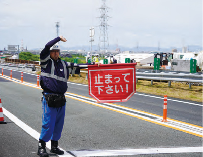 停止旗を掲げて緊急車両の通行を誘導する交通管理員